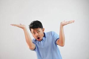 joven asiático hombre interino me gusta él es participación arriba alguna cosa pesado, pero es sólo vacío Copiar espacio vistiendo azul t camisa aislado en blanco antecedentes. conmocionado cara foto