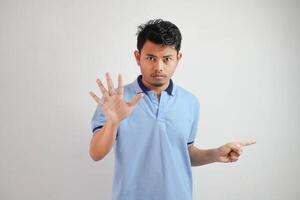 atractivo asiático hombre con mano gesto actitud rechazo o prohibición mientras señalando a Copiar espacio por su lado vistiendo azul t camisa aislado en blanco antecedentes foto