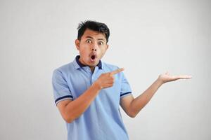 conmocionado asiático hombre con un abierto mano con dedos señalando a el lado vistiendo azul t camisa aislado en blanco antecedentes foto