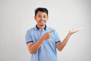 sonriente asiático hombre con un abierto mano con dedos señalando a el lado vistiendo azul t camisa aislado en blanco antecedentes foto