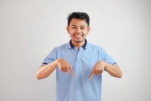 excited young asian man looking camera finger pointing downwards wearing blue t shirt isolated on white background photo