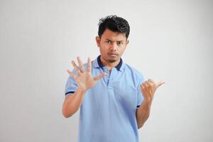 atractivo asiático hombre con mano gesto actitud rechazo o prohibición mientras señalando a Copiar espacio por su lado vistiendo azul t camisa aislado en blanco antecedentes foto