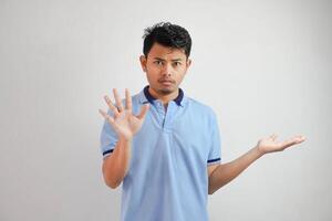 Attractive Asian man with hand gesture pose rejection or prohibition while pointing to copy space by his side wearing blue t shirt isolated on white background photo