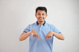 emocionado joven asiático hombre mirando cámara dedo señalando hacia abajo vistiendo azul t camisa aislado en blanco antecedentes foto