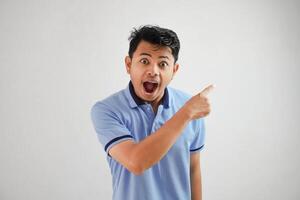 shocked asian man with an open mouth with fingers pointing to the side wearing blue t shirt isolated on white background photo