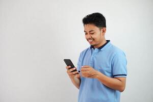 sonriente o contento joven hermoso asiático hombre participación teléfono vistiendo azul t camisa aislado en blanco antecedentes foto