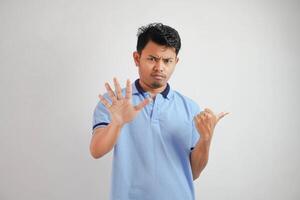 atractivo asiático hombre con mano gesto actitud rechazo o prohibición mientras señalando a Copiar espacio por su lado vistiendo azul t camisa aislado en blanco antecedentes foto