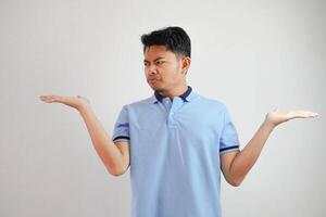 grave cara asiático hombre con ambos brazos abierto a vacío espacio junto a él vistiendo azul t camisa aislado en blanco antecedentes foto