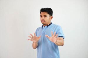 atractivo asiático hombre con mano gesto actitud rechazo o prohibición mientras señalando a Copiar espacio por su frente vistiendo azul t camisa aislado en blanco antecedentes foto