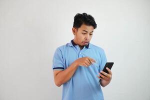 portrait asian man shocked holding phone and pointing at the phone with a finger wearing blue polo t shirt isolated on white background photo