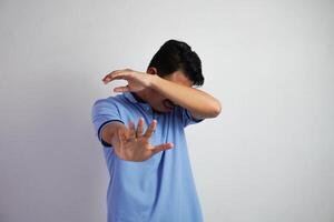 atractivo asiático hombre con mano gesto actitud rechazo o prohibición mientras señalando a Copiar espacio por su lado vistiendo azul t camisa aislado en blanco antecedentes foto