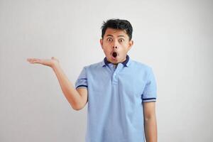 conmocionado asiático hombre con un abierto mano con dedos señalando a el lado vistiendo azul t camisa aislado en blanco antecedentes foto