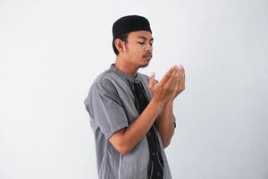 religioso joven asiático musulmán hombre con cerca ojos Orando, participación palmas cara arriba, susurro orar, aislado en blanco antecedentes. religión islam, creyendo concepto foto