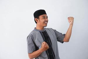 Successful happy young asian muslim man screaming shouting and shows winning victory gesture wearing grey muslim clothes isolated on white background photo