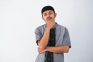 thinking young asian muslim man holding chin thinking gesture, looking for idea wearing grey muslim clothes isolated on white background photo