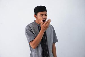 young Asian muslim man having bad breath problem during fasting in ramadan moth wearing grey muslim clothes isolated on white background photo