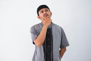 thinking young asian muslim man holding chin thinking gesture, looking for idea wearing grey muslim clothes isolated on white background photo