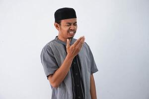 joven asiático musulmán hombre teniendo malo aliento problema durante rápido en Ramadán polilla vistiendo gris musulmán ropa aislado en blanco antecedentes foto