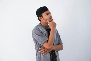 pensando joven asiático musulmán hombre participación barbilla pensando gesto, mirando para idea vistiendo gris musulmán ropa aislado en blanco antecedentes foto