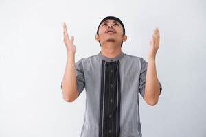 Religious young asian muslim man with open eyes praying, holding palms face up, whispering pray, isolated on white background. Religion islam, believing concept photo