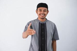 sonriente asiático musulmán hombre simpático ofrecimiento apretón de manos como saludo y acogedor exitoso negocio.vistiendo gris koko ropa aislado en blanco antecedentes foto
