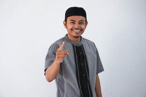 young asian muslim man smile pointing his both finger to camera wearing grey muslim clothes isolated on white background photo