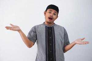 joven asiático musulmán hombre elevado brazos y mirando a cámara con dudoso cara vistiendo koko ropa aislado en blanco antecedentes. foto