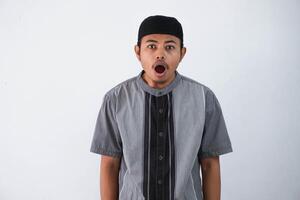 shocked young asian muslim man open mouth can not believe of what he sees. Worried expression wearing koko clothes isolated on white background photo