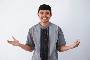 smiling or happy young asian muslim man greeting during Ramadan celebration with both arms open wearing grey muslim clothes isolated on white background photo