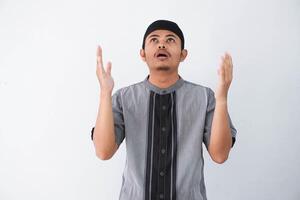 Religious young asian muslim man with open eyes praying, holding palms face up, whispering pray, isolated on white background. Religion islam, believing concept photo