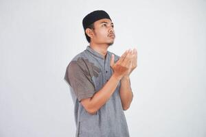 Religious young asian muslim man with open eyes praying, holding palms face up, whispering pray, isolated on white background. Religion islam, believing concept photo