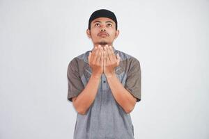 Religious young asian muslim man with open eyes praying, holding palms face up, whispering pray, isolated on white background. Religion islam, believing concept photo