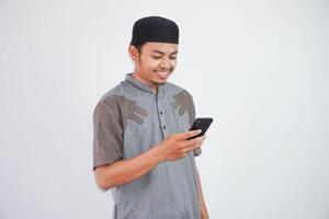 Happy or smiling young asian muslim man holding phone cellular wearing koko clothes isolated on white background. Ramadan concept photo