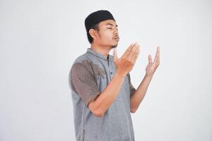 Religious young asian muslim man with close eyes praying, holding palms face up, whispering pray, isolated on white background. Religion islam, believing concept photo