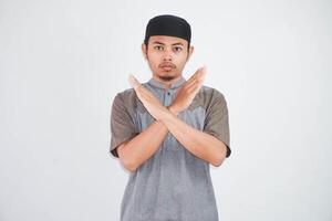 Serious young Asian Muslim man crossing hands makes stop gesture and demonstrates rejection wearing kurta clothes isolated on white background photo