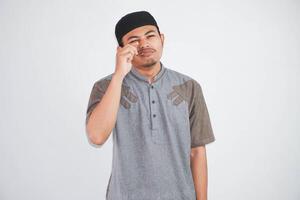joven asiático musulmán hombre frota lágrimas quiere a llorar sensación Deprimido tiene un problema vistiendo musulmán ropa aislado en blanco antecedentes foto