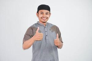 smiling or happy young muslim man showing hand thumbs up wearing grey muslim clothes isolated on white background photo