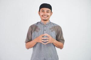 Smiling Asian Muslim man holding hands together and feels optimistic wearing muslim clothes isolated on white background photo