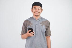 Happy or smiling young asian muslim man holding phone cellular wearing koko clothes isolated on white background. Ramadan concept photo