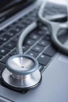 Closeup Grey Stethoscope on laptop keyboard. Health care or IT security concept. photo