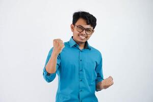 Excited young asian businessman with glasses in wearing blue shirt standing doing winner gesture clenching fists isolated on white background photo