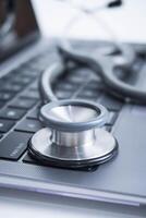 Closeup Grey Stethoscope on laptop keyboard. Health care or IT security concept. photo