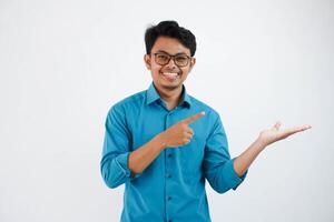 sonriente asiático empresario con un abierto mano con dedos señalando a el lado vistiendo azul camisa aislado en blanco antecedentes foto