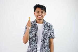 sonriente o contento joven asiático hombre participación maquinilla de afeitar en pie y mirando cámara aislado en blanco antecedentes foto