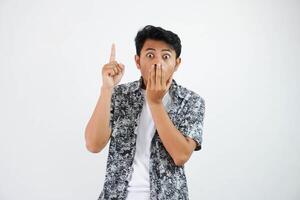 shocked young asian man pointing up finger and close the mouth isolated on white background photo