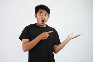 shocked asian man with fingers pointing to the side wearing black t shirt isolated on white background photo