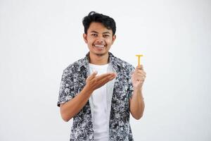 sonriente o contento joven asiático hombre señalando a el maquinilla de afeitar con su dedo vistiendo negro camisa aislado en blanco antecedentes foto