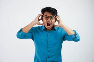 shouted or shocked young asian businessman with glasses holding head with mouth open wearing blue shirt isolated photo