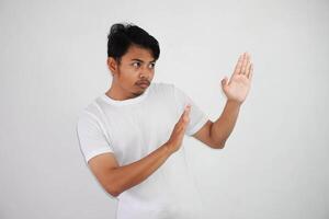 Displeased handsome young asian man wearing white t shirt showing stop sign isolated on white background photo