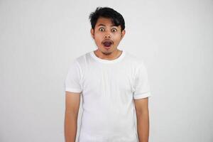 Close up of shocked young Asian man with open mouth and looking at camera wearing white t shirt isolated on white background photo